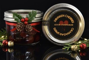 Small mason jars of cherries are decorated with holly for Christmas.