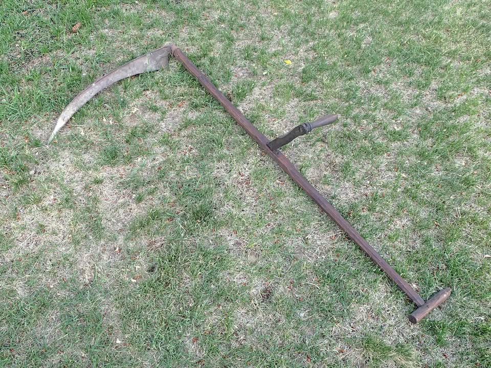 An old scythe lies on a lawn.