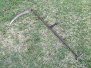 An old scythe lies on a lawn.