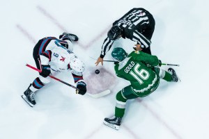 Hockey players facing off as a referee drops the puck.