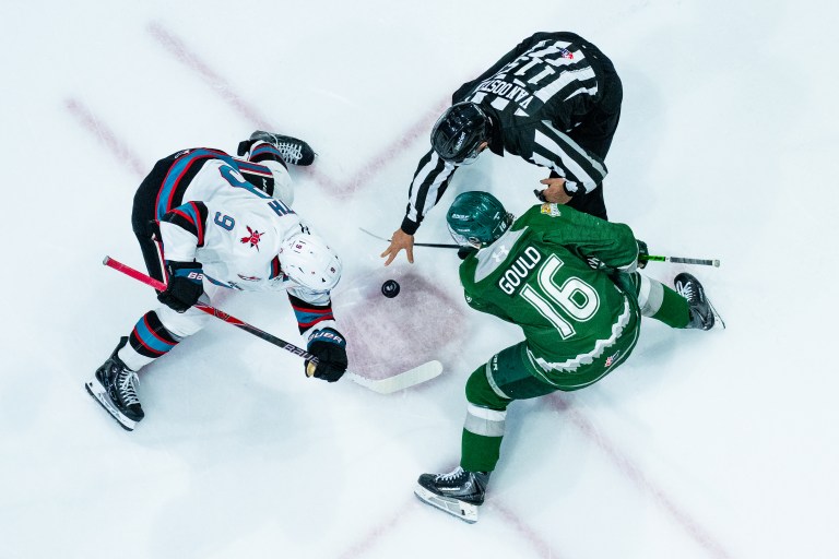 Hockey players facing off as a referee drops the puck.