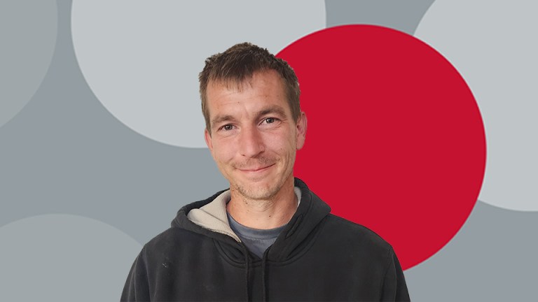A man smiling in front of a grey background.