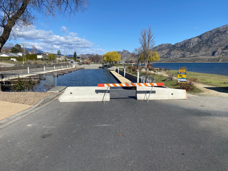 A road barrier blocking access to a boat launch on a sunny day.