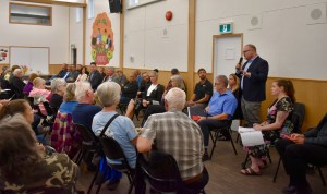 A group of seniors listen to a man speaking into a microphone.