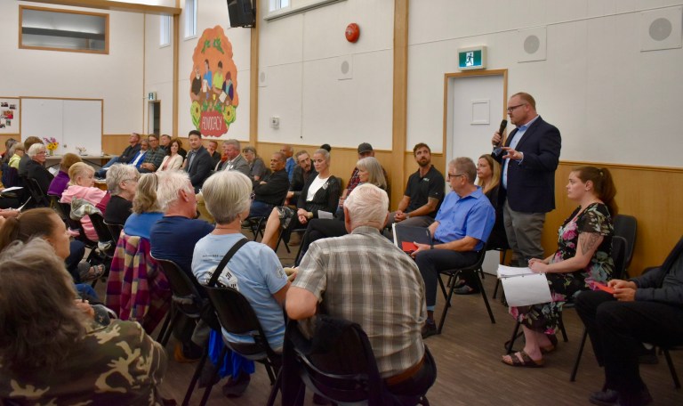 A group of seniors listen to a man speaking into a microphone.