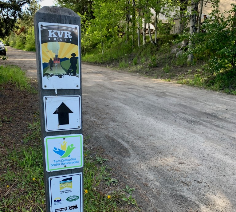 A sign along a trail surrounded by trees.
