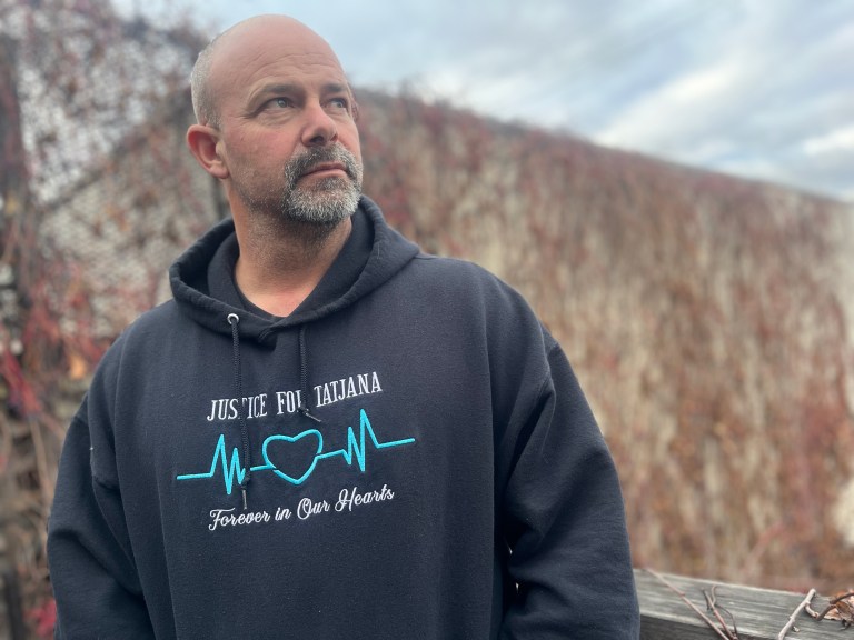 A man in a hoodie stands on a patio and looks towards the sky.