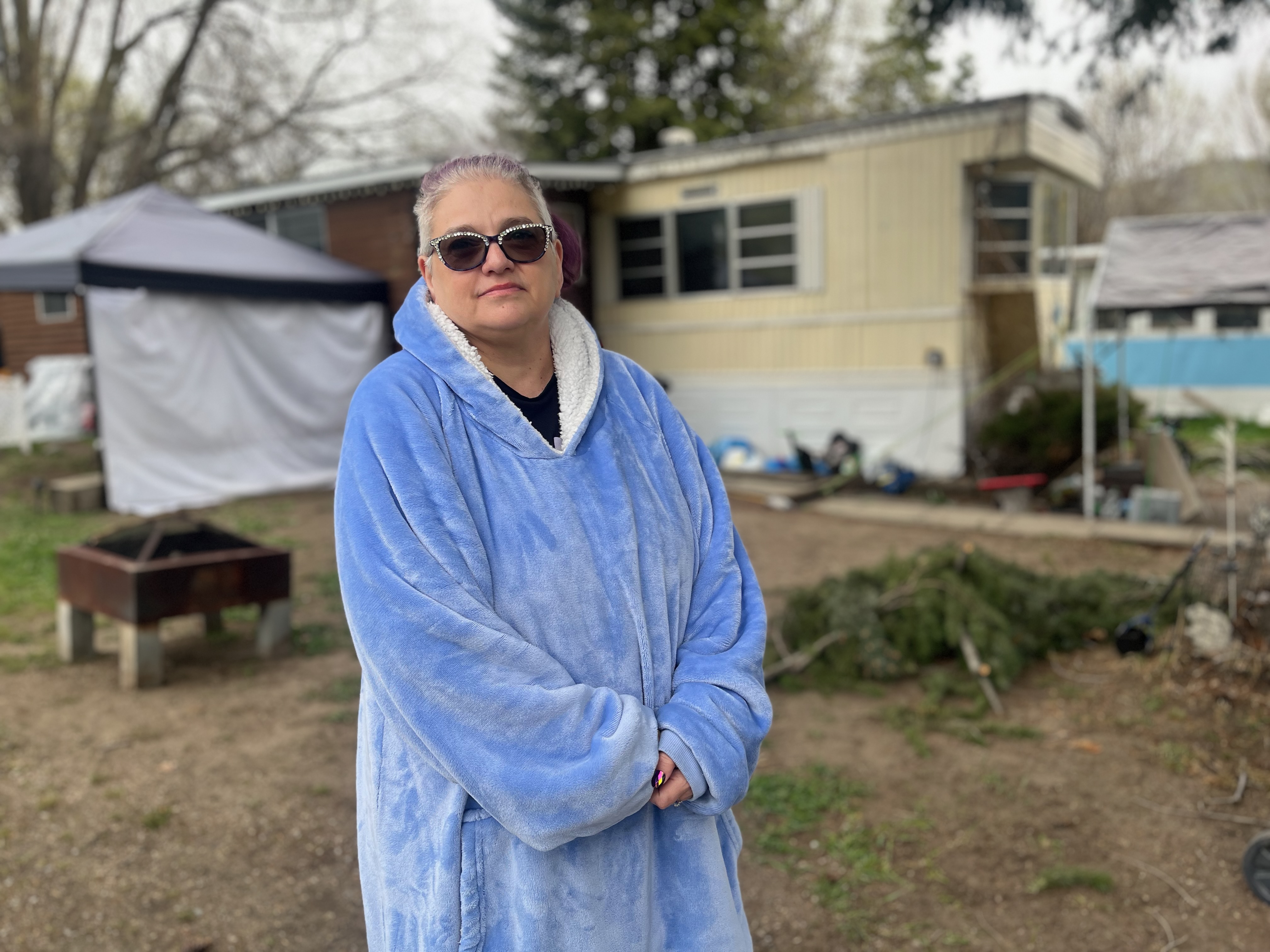 Lisa Cantafio-Anderson wears a blue coat and stands outside a mobile home.