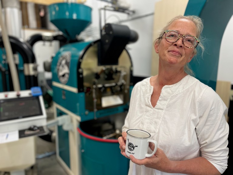 A woman stands in front of a lot of boxes holding a mug of coffee.