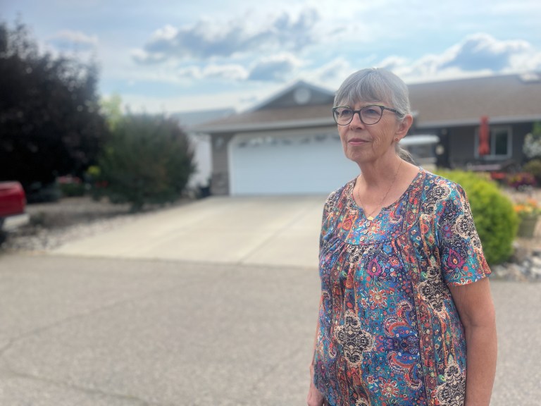 A woman stands outside her home.
