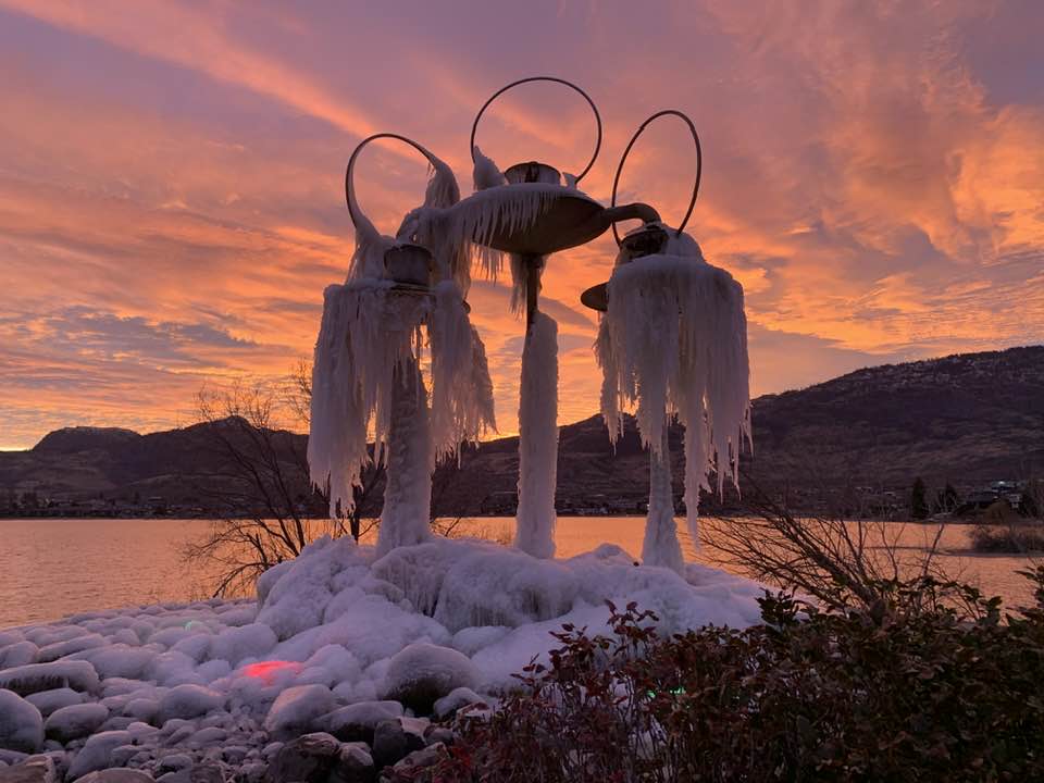 Fountain is covered with icicles with a sunset behind it.