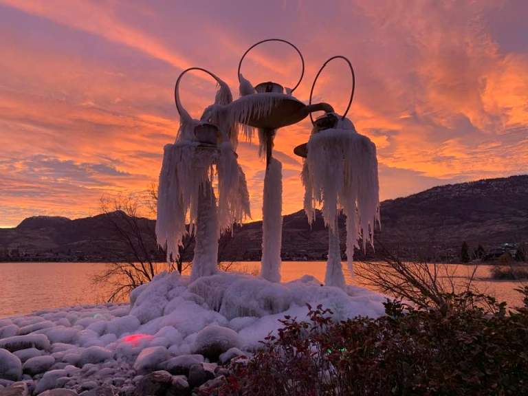 Fountain is covered with icicles with a sunset behind it.