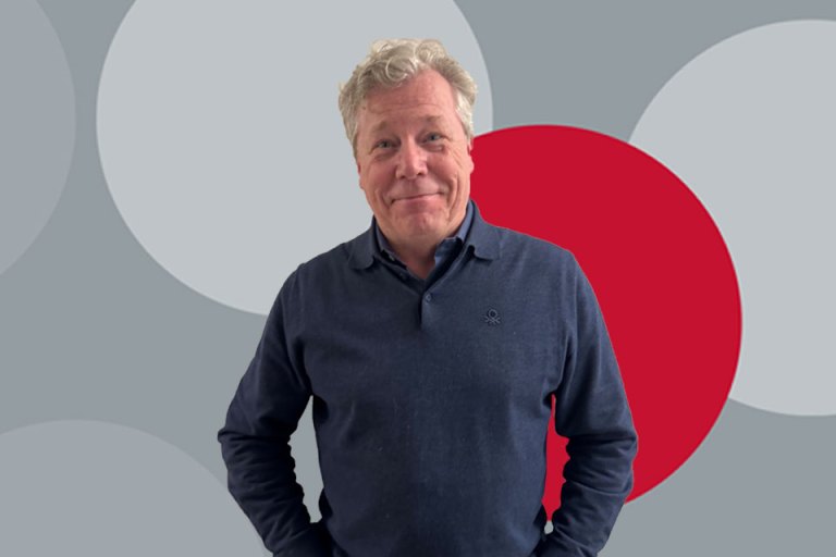 A man in a blue shirt in front of a grey and red background.