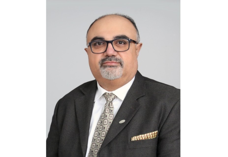 This photo is a headshot of a man wearing a suit and glasses.