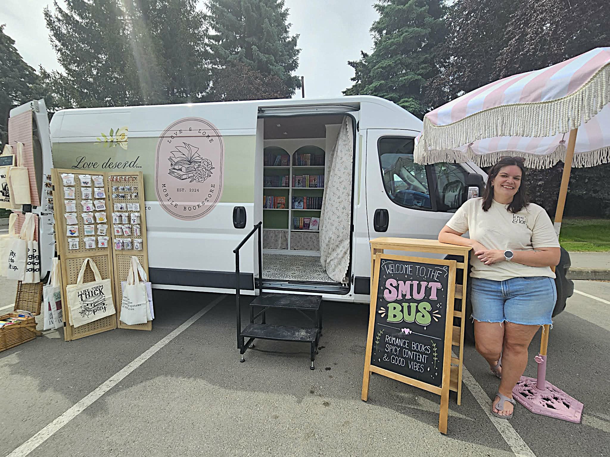 A woman stands next to a sandwich board in front of a mobile bookstore.
