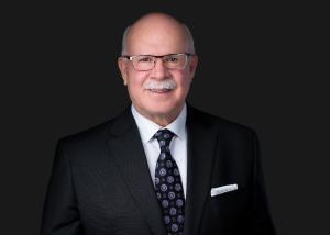 A senior in a dark suit in front of a dark background.