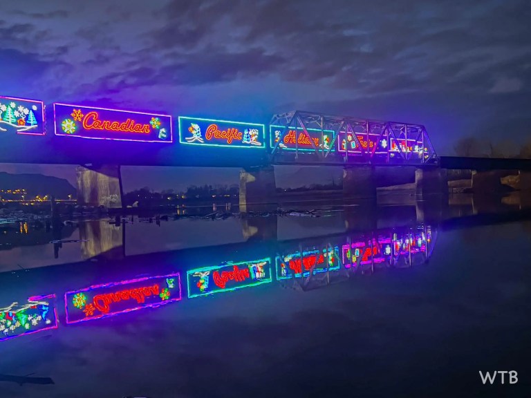 A holiday-themed train crosses a bridge over a river at night.
