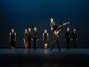 Several ballet dancers in black performing on stage.