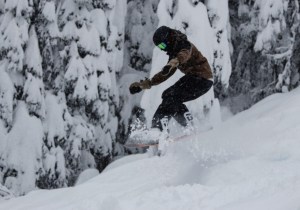 A snowboarder jumping through some powder.