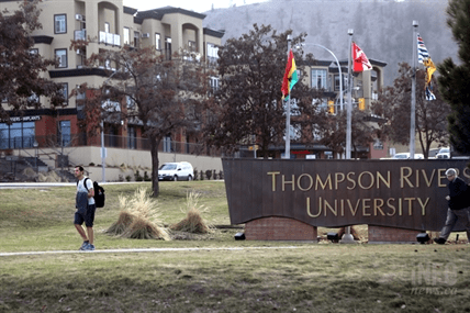 A man walks by a university entrance sign on a grass lawn.