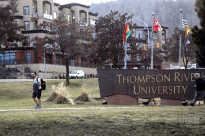 A man walks by a university entrance sign on a grass lawn.