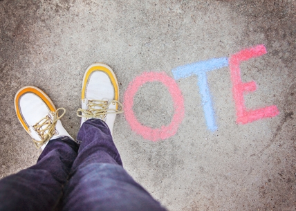 A person uses their shoes to make the V in the chalk written word vote on pavement.