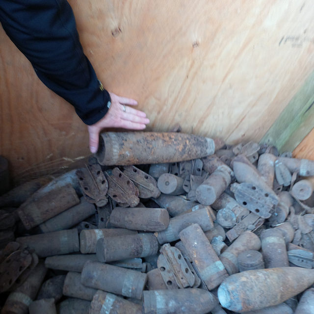 An arm and hand touches a pile of unexploded military ordnance.
