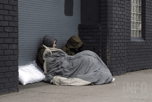 Two people under a blanket on a sidewalk.