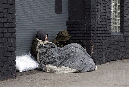 Two people under a blanket on a sidewalk.