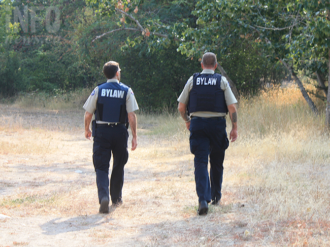 Two Penticton bylaw officers walking through a park.