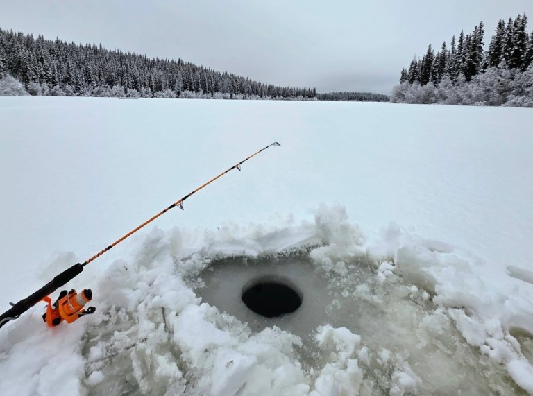 A fishing rod lies beside a hole in the ice in a lake.