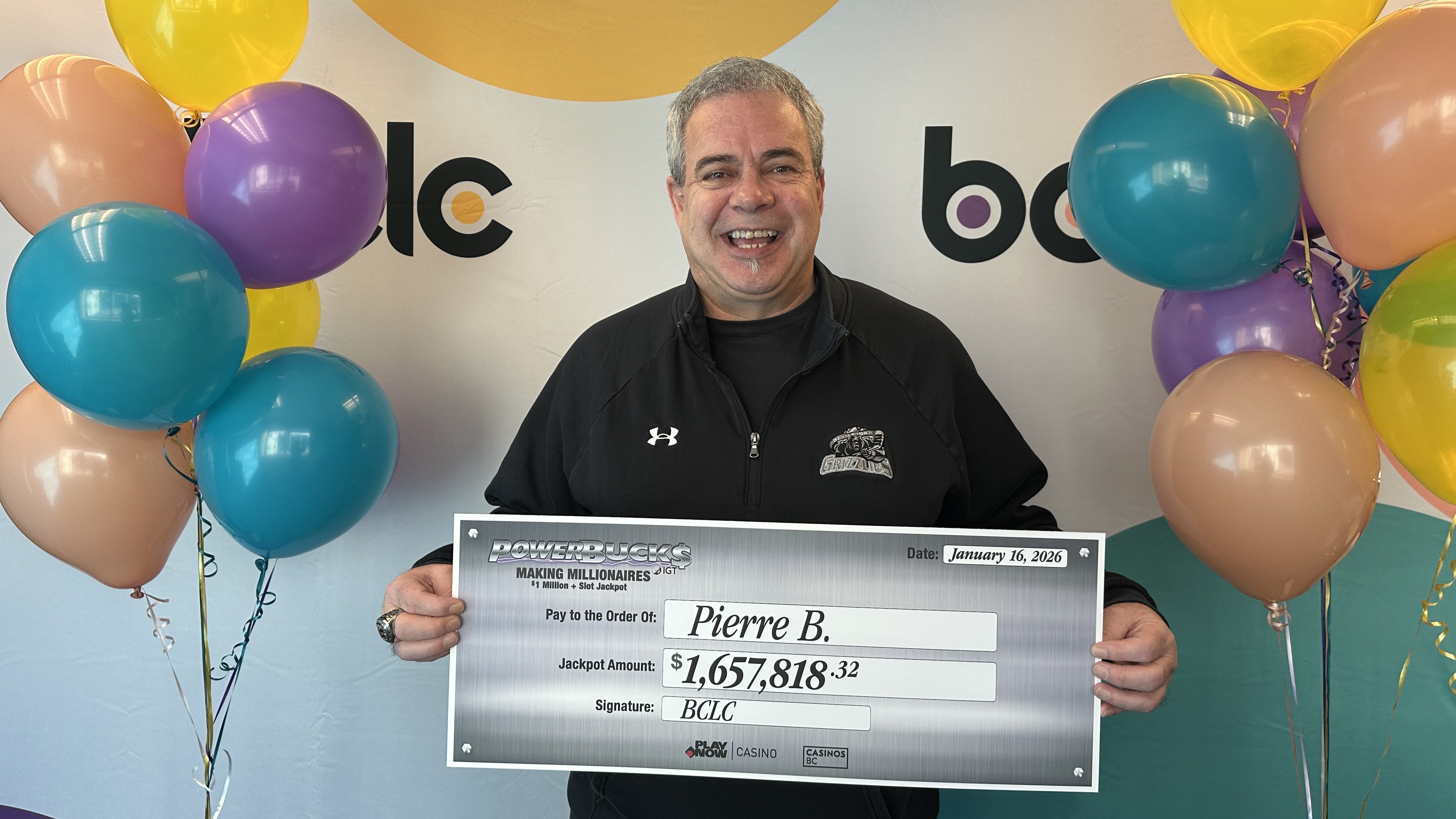 A man holds a big check from BCLC surrounded by balloons.