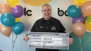 A man holds a big check from BCLC surrounded by balloons.