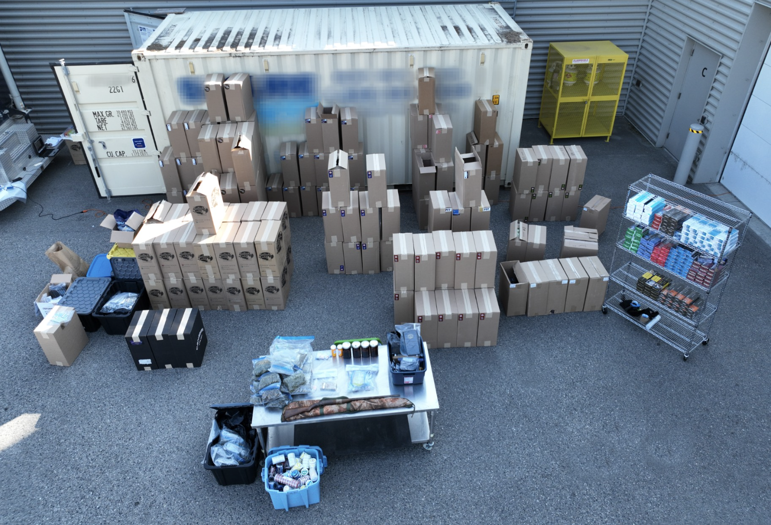 Boxes filled with cigarettes and drugs next to a shipping container.
