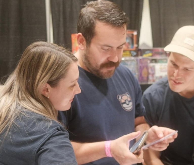 Two people looking at someone going through Pokèmon cards.