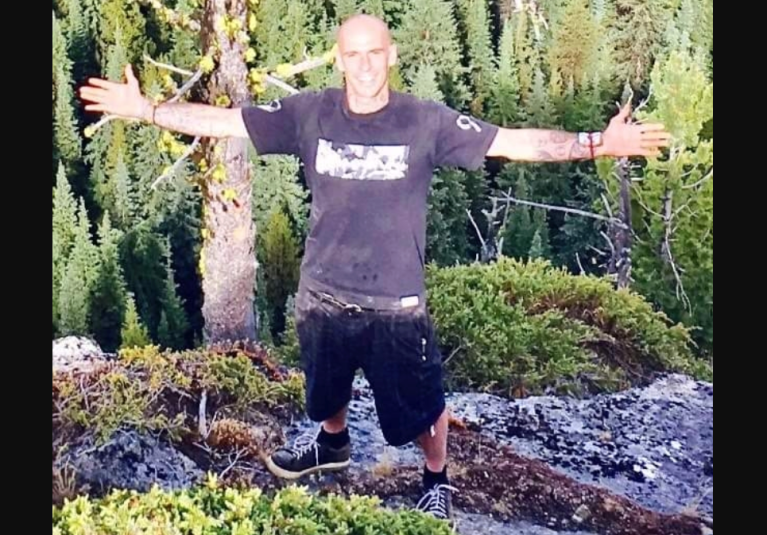 Bail denied for Okanagan man who allegedly started Knox Mountain blaze | iNFOnews.ca A man stands in a wooded area with his arms outstretched.