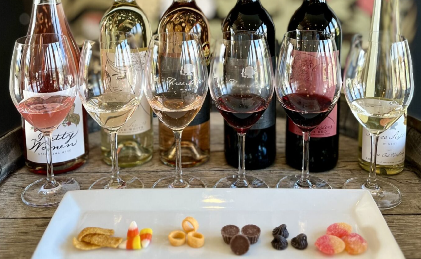 Five glasses of wine with pieces of candy laid out in front.