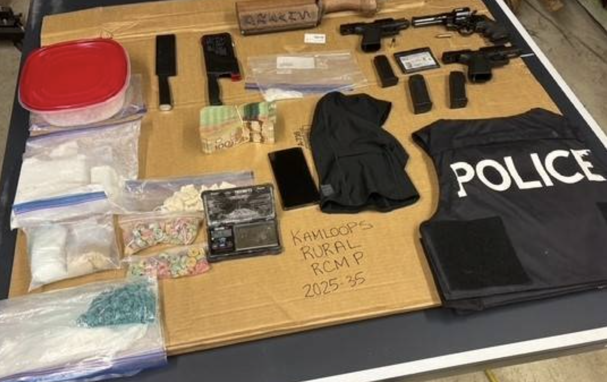 Drugs and guns laid out on a table with a police vest.