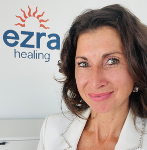 Ezra Healing owner Svetlana Rilkoff poses for a selfie with her businesses sign behind her.