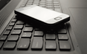 A cell phone rests on the keyboard of a laptop computer.