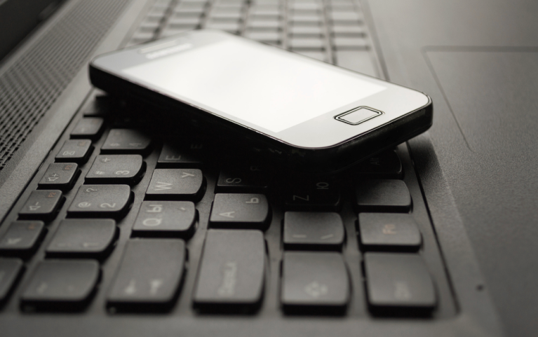 A cell phone rests on the keyboard of a laptop computer.