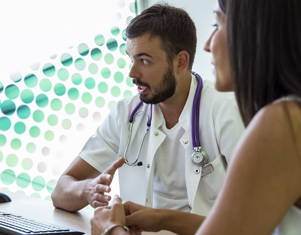 A doctor with a stethoscope speaking with a woman.