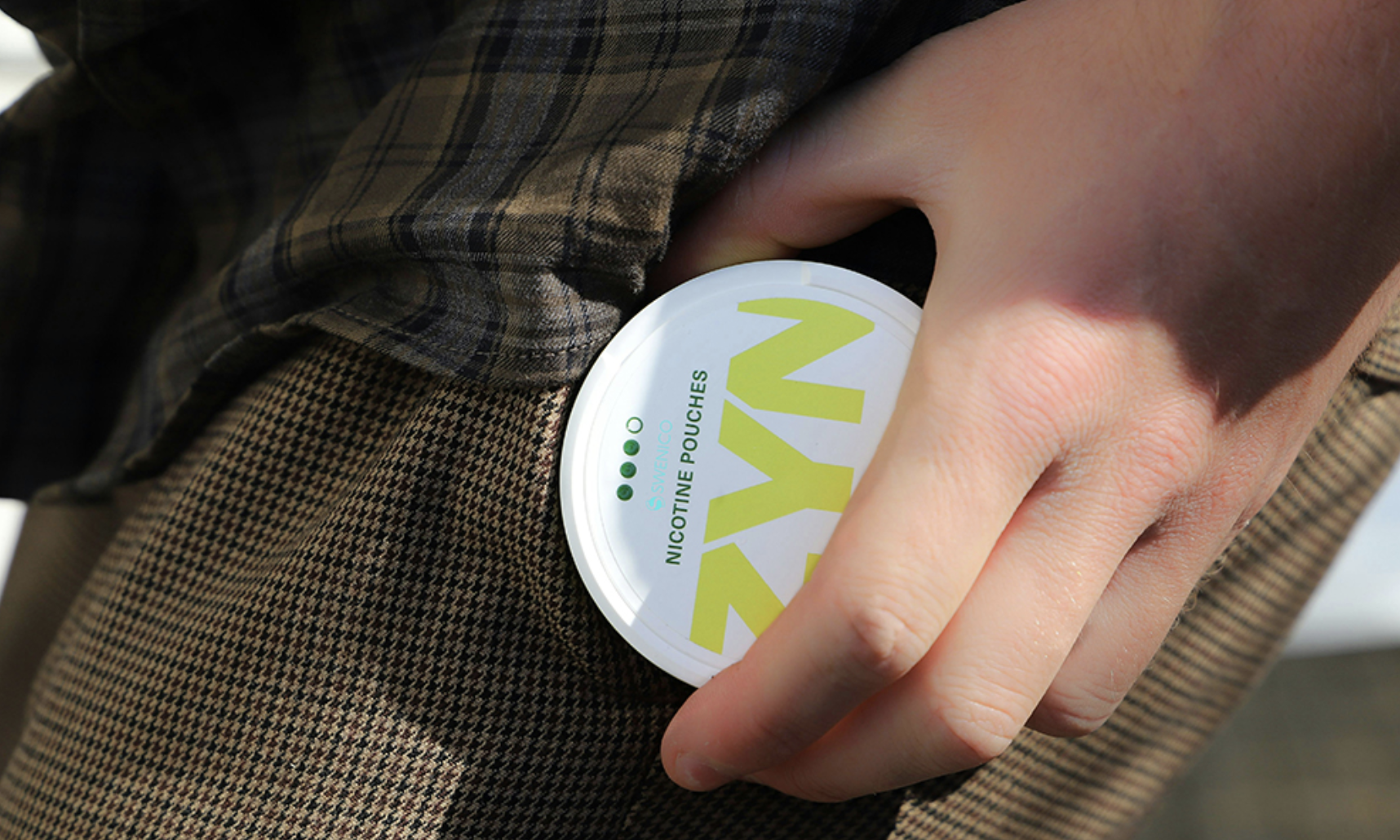 Someone putting a container of nicotine pouches in their pocket.