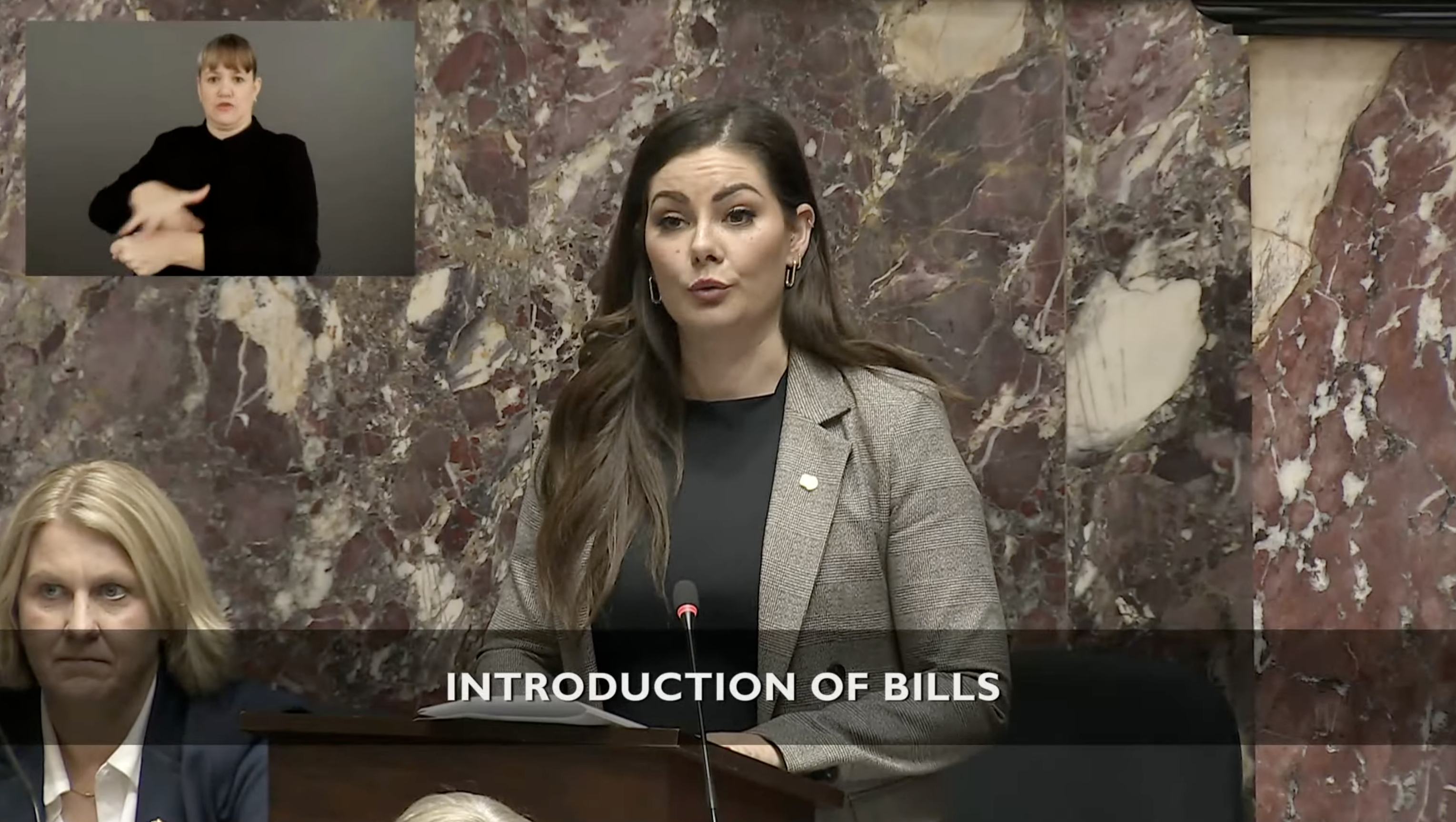 Amelia Boutlbee stands at her desk in the legislature.