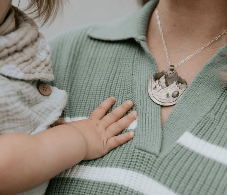 A woman holding a toddler while wearing a necklace of mountains.