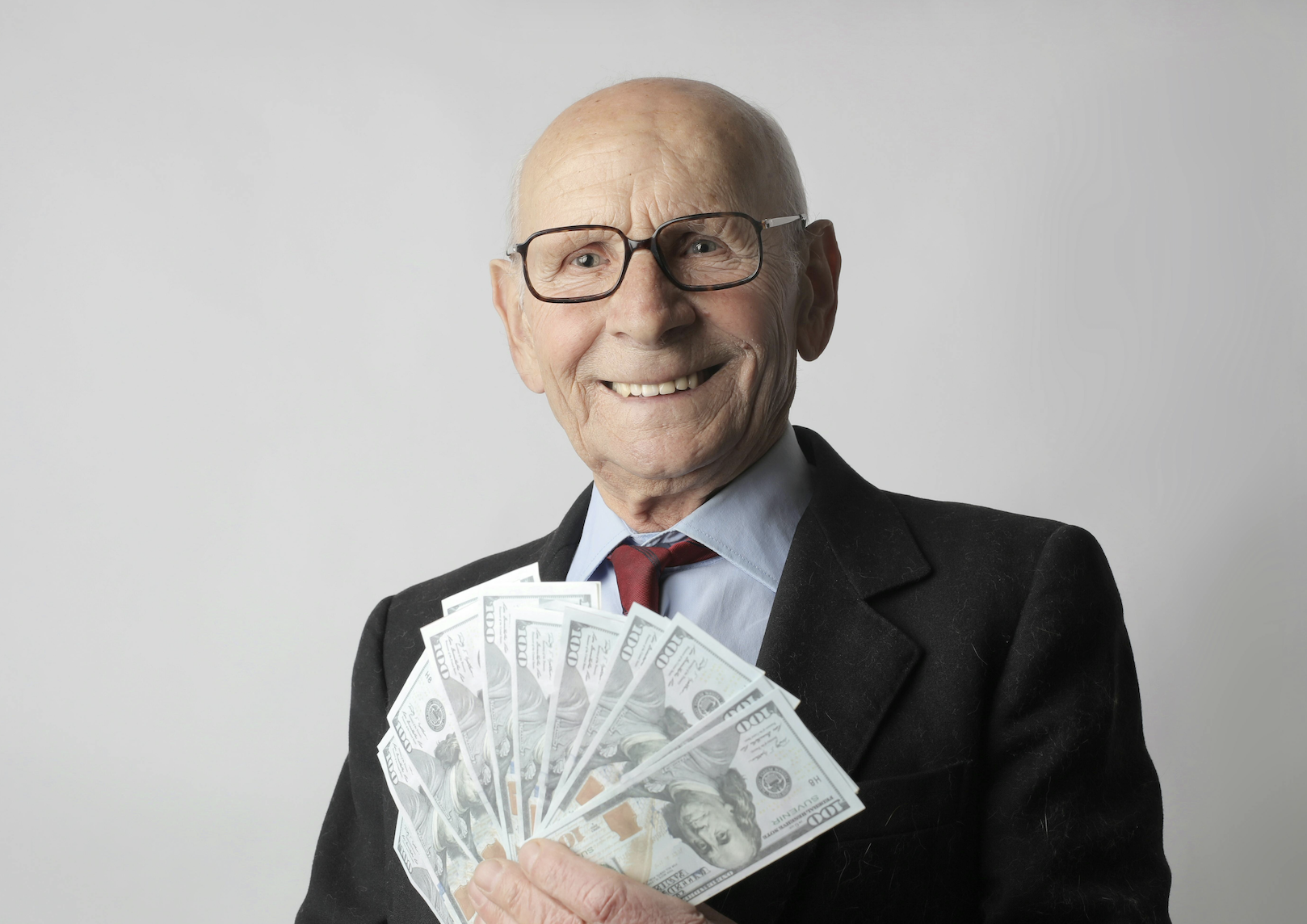 A bald elderly man fans out American cash in his hand.