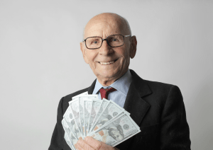 A bald elderly man fans out American cash in his hand.