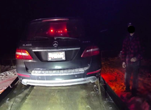 A man next to a Mercedes being loaded onto a tow truck.