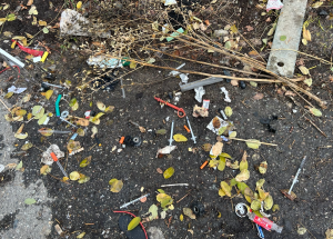 A bunch of needles, broken pipes and garbage on the ground.