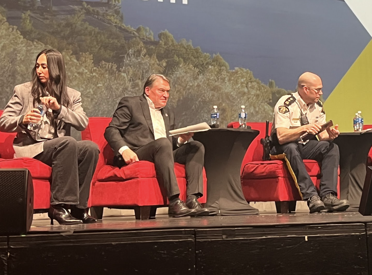 Three people in red chairs on a stage.